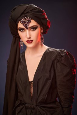 Geleneksel makyajlı, siyah sarıklı ve takılı çekici bir doğulu kadın siyah arka planda poz veriyor. Makyaj ve kozmetik. 