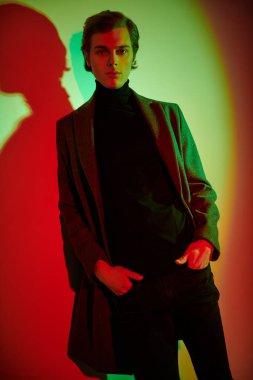 Stüdyoda renkli ışıkta şık kıyafetler içinde poz veren zarif bir gencin portresi. Moda fotoğrafı..