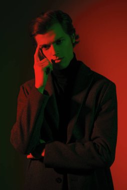 Zarif elbiseli düşünceli yakışıklı genç adam stüdyoda kırmızı ve yeşil ışıkta poz veriyor. Erkek stili. 