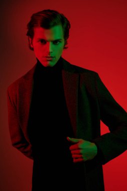 Zarif elbiseli şık genç adam stüdyoda kırmızı ve yeşil ışıkta poz veriyor. Erkek stili. 