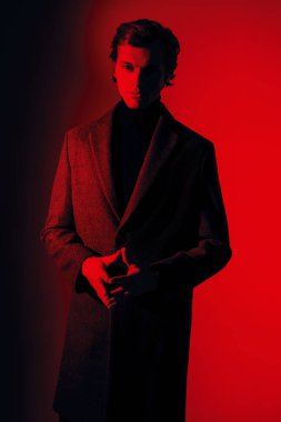 Şık giyinmiş yakışıklı erkek model stüdyoda kırmızı ışıkta poz veriyor. Erkek stili ve modası. 