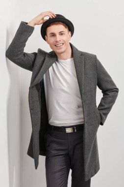 Zarif bir ceket ve şapkası olan orta yaşlı yakışıklı bir adam beyaz bir duvarın yanında duruyor ve gülümsüyor. Erkek güzelliği, moda. Yaşam tarzı. Hippi adam.. 