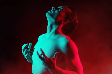 Athletic young man shirtless expressive poses in red and green light. Man's beauty and health. Art portrait.