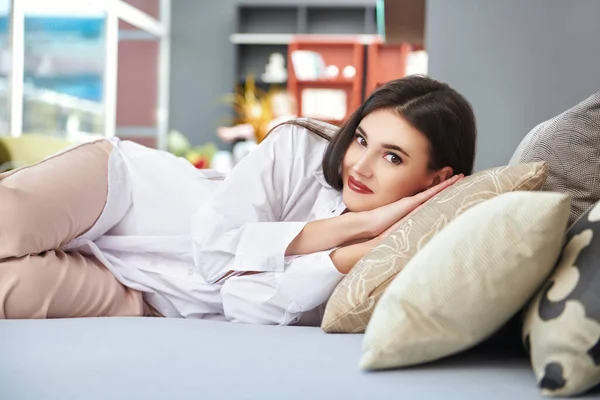 Happy young woman lay down to rest on the bed in her cozy studio apartment. Happy people and lifestyle concept.