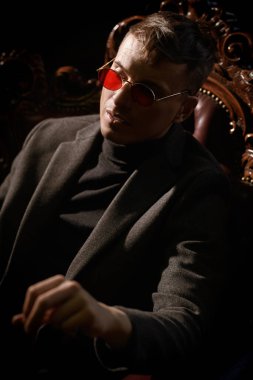 Pahalı kıyafetler ve gözlüklerle donatılmış otoriter olgun bir adam lüks bir dairede koltukta oturuyor. Mafya, gangster adam.. 