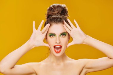 Renkli makyajlı, sarı arka planda ifadesiyle poz veren çekici ve etkileyici bir kızın portresi. Makyaj ve makyaj malzemeleri. İnsani duygular. Boşluğu kopyala. 