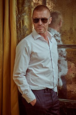 Lüks bir dairede, beyaz gömlekli ve modern güneş gözlüklü, çok zengin bir adamın portresi. Erkek güzeli, moda. Optik, erkekler için güneş gözlüğü..