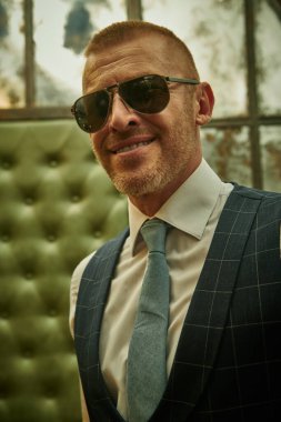 Lüks bir dairede duran şık takım elbiseli, olgun, yakışıklı bir adamın portresi. Erkek güzeli, moda. Optik, erkekler için güneş gözlüğü..