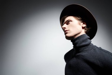 Sanat portresi. Geniş kenarlı şapkalı ve balıkçı yaka kazaklı yakışıklı bir genç. Kopyalama alanı olan gri arkaplan. 