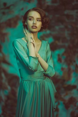 Saçları ve makyajı 20 'li yılların tarzında. Zarif elbiseli, sofistike bir kız eski bir duvarın arkasında duruyor. Sanat modası. 