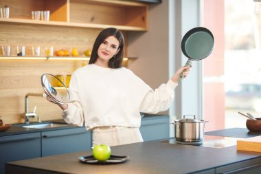 Mutfakta elinde tavayla durup gülümseyen mutlu esmer kız. Sağlıklı beslenme ve beslenme. Modern iç mekan, mutfak mobilyası..