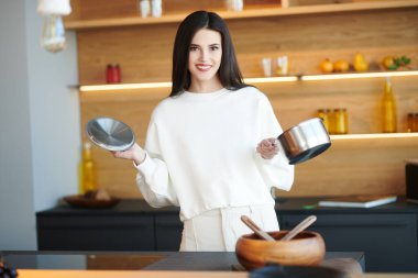 Güzel esmer kız elinde çorba güveciyle mutfakta duruyor ve gülümsüyor. Sağlıklı beslenme ve beslenme. Modern iç mekan, mutfak mobilyası..