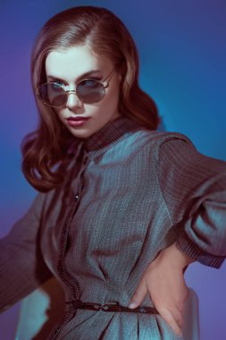 Koyu mavi arka planda zarif gözlüklü güzel bir genç kadının portresi. Gözlük modası. 