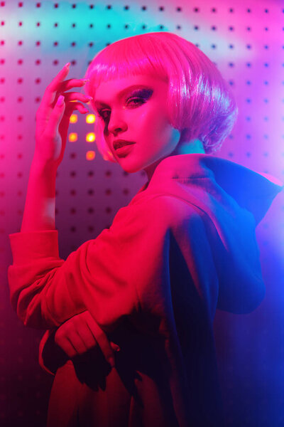 Портрет современной девушки с ярким блестящим макияжем и розовыми волосами, позирующими в неоновых огнях ночного клуба. Диско стиль. Ночная вечеринка. 