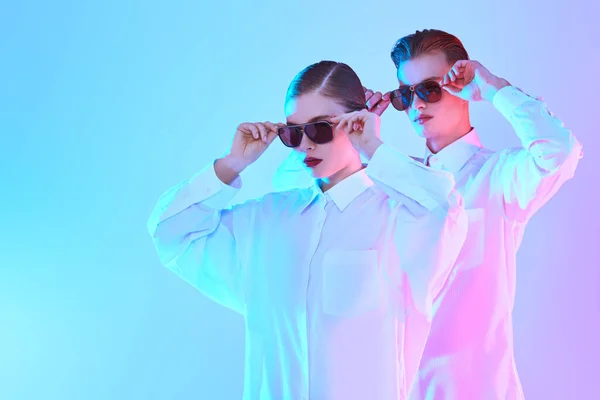 Fashion girl and guy posing in white shirts and modern sunglasses are pose at studio. Optics, fashion.