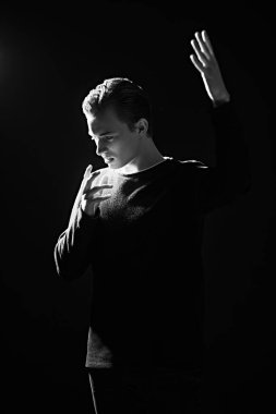 Siyah-beyaz bir portre. Stüdyoda karanlık ışıkta ifade ile poz veren cesur bir genç. Erkek güzelliği. Siyah arkaplan. 