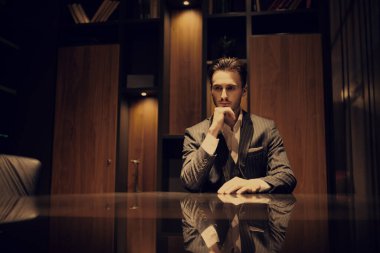 Zarif takım elbiseli yakışıklı esmer adam lüks bir dairede oturuyor. - Mafya. Erkek güzelliği, moda.