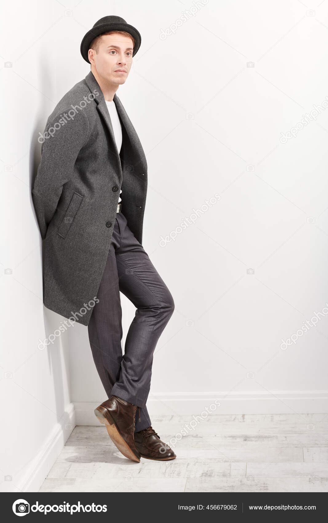一位中年男子的全长画像他身穿雅致的外套头戴一顶帽子站在一面白墙旁边男人的美希斯特男人混光下的工作室肖像