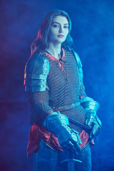 A beautiful noble warrior woman in chain mail and plate armor poses holding her sword. Medieval knight.