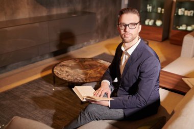 Zarif klasik takım elbiseli ve gözlüklü saygıdeğer orta yaşlı işadamı modern dairelerde kitap okuyor. Başarılı yönetici kavramı.