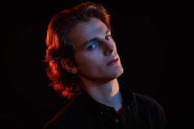 Siyah arka planda dalgalı saçlı, karışık renkli ışık saçan yakışıklı bir gencin portresi. Erkek güzelliği. Boşluğu kopyala.