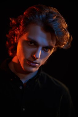 Siyah arka planda dalgalı saçlı, karışık renkli ışık saçan yakışıklı bir gencin portresi. Erkek güzelliği. Boşluğu kopyala.