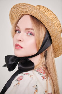Hasır şapkalı güzel sarışın kız ve beyaz arka planda bir yaz bluzu. Pembe renkli açık renk makyaj. Bahar ve yaz güzelliği. Moda.. 