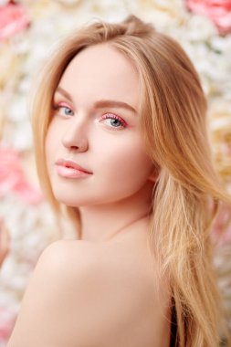 Açık makyajlı, pembe renkli ve sarı saçlı, çiçek açan güllerin arka planında çekici bir genç kadın. Bahar kızı. Güzellik konsepti. 