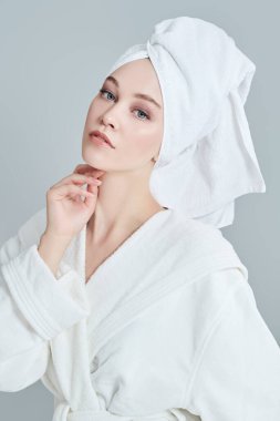 Beyaz bornozlu güzel bir genç kadın portresi ve duş aldıktan sonra saçının etrafına bir havlu. Güzellik, vücut bakımı, kaplıca.