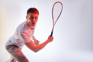 Duygusal sporcu adam beyazın üstünde zevkle squash oynar. Aktif yaşam tarzı. Spor ve sağlık hizmetleri. Stüdyo resmi kırmızı ışıkta. 