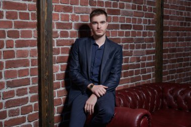 Yakışıklı, olgun bir adam duvardaki deri koltukta oturur. Erkek güzelliği, moda.