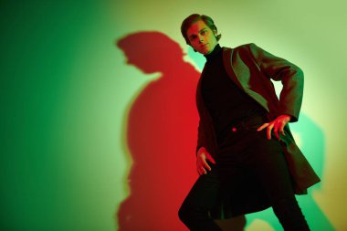 Stüdyoda renkli ışıkta şık kıyafetler içinde poz veren zarif bir gencin portresi. Moda fotoğrafı..