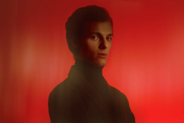 Zarif elbiseli yakışıklı genç adam stüdyoda kırmızı ışıkta puslu poz veriyor. Erkek stili. 