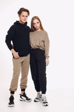 Modern gençlerin tam boy portresi. Stüdyoda bej ve siyah spor kıyafetleriyle poz veren bir kız ve bir erkek. Spor stili. 
