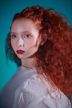 Beyaz bir sanat elbisesi içinde poz veren gür kıvırcık saçlı kızıl saçlı kadın modelin yakın portresi. Yüksek moda sanatı. 