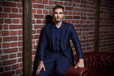 Duvarda, deri koltuğun yanında oturan yakışıklı, olgun bir adamın portresi. Erkek güzelliği, moda.