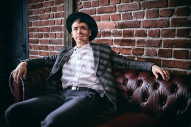 Zarif kıyafetleri ve şapkası olan hayalperest orta yaşlı bir adam bir çatı katındaki bir dairede, aydınlık ve gölgede, deri bir koltukta rahatça oturuyor. Erkek güzelliği, moda. Yaşam biçimi. 