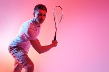 Heyecanlı sporcu heyecanla squash oynuyor. Aktif yaşam tarzı. Spor ve sağlık hizmetleri. Stüdyo portresi ve karışık renkli ışık. Boşluğu kopyala. 