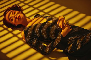 Gece elbisesi giymiş güzel bir kız gün batımının gölgesinde yerde yatıyor. Saçları ve makyajı 20 'li yılların tarzında. Sanat modası. 