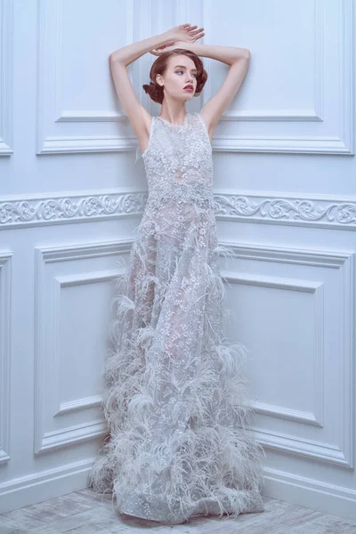 Beyaz bir gelinlik içinde beyaz bir odada klasik iç mimari ile poz veren çarpıcı genç bir kadının tam boy portresi. Moda fotoğrafı. Gelinlik.