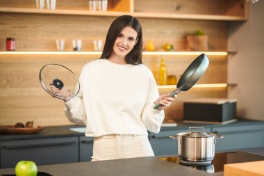 Mutfakta elinde tavayla durup gülümseyen mutlu esmer kız. Sağlıklı beslenme ve beslenme. Modern iç mekan, mutfak mobilyası..