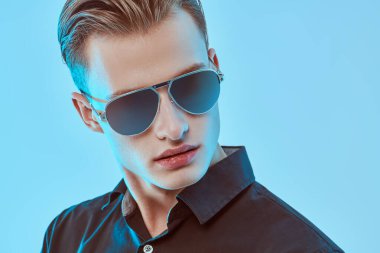 Koyu renk bir gömlek ve modern güneş gözlüğü takan şık bir genç adam. Erkek aksesuarları, optikler. Stüdyo resmi.