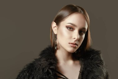Stüdyoda siyah elbiseler ve siyah kürk mantoyla gri arka planda kar altında poz veren çekici bir manken. Güzellik, moda.
