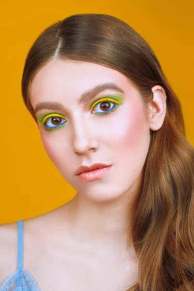 Makyaj ve makyaj malzemeleri. Sarı arka planda parlak renkli makyajlı güzel bir kızın yakın plan portresi..