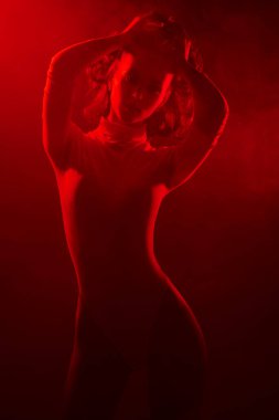 Duman içinde kırmızı ışıkta beyaz tulumla poz veren ince vücutlu güzel bir manken kızın sanat portresi. Moda stüdyosu çekimi. 