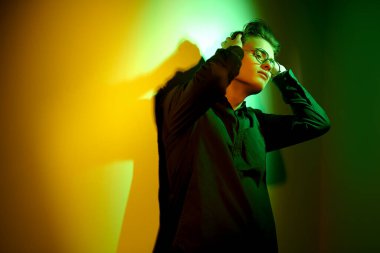 Yakışıklı genç adam ayakta duruyor, üzgün ve yalnız, ellerini tutarak duvara yaslanmış koyu yeşil ve sarı ışıkta. Duygular ve duygular. 