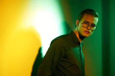 Yakışıklı genç adam poz veriyor ve dikkatlice duvara bakıyor. Koyu yeşil ve sarı ışıklandırmalı..  