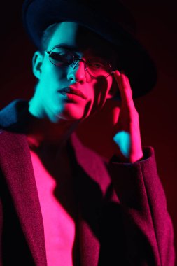 Ceket, şapka ve gözlük takan yakışıklı bir manken ve yeşil ışık. Erkekler için optik. Erkek modası. Portreyi kapat.