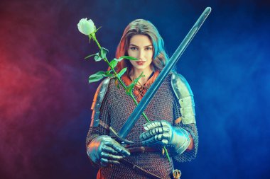 A beautiful and strong woman knight in armor holds a tender white rose and sword in her iron gloves. Middle Ages. clipart