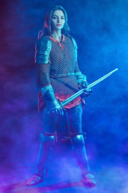 Güzel bir ortaçağ kadın şövalyesinin koyu mavi dumanlı arka planda tam boy portresi..